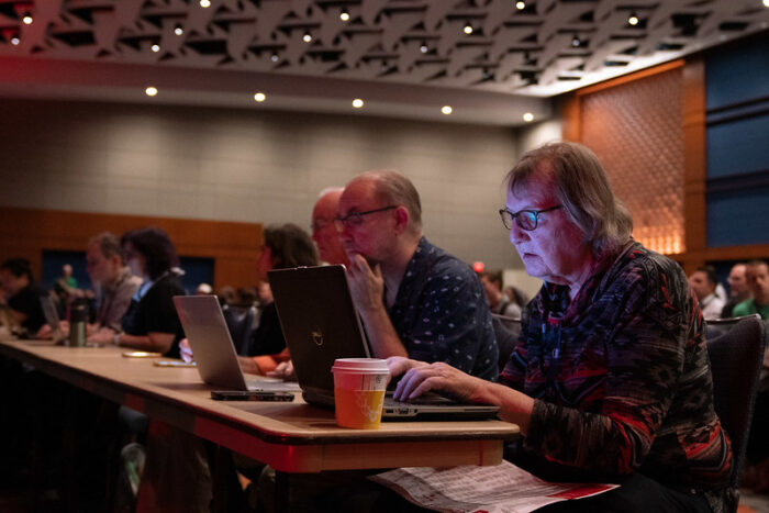 FOSS Force tech journalist Christine Hall sitting at a press table typing on a laptop during the opening keynotes at ATO 2019.