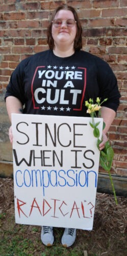 "You're in a Cult "T-shirt on woman carrying sign.
